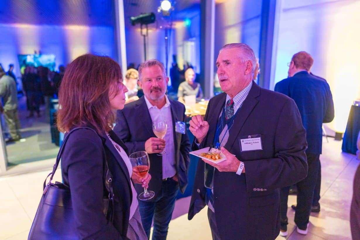 two men and women talking, eating, drinking, standing while at an event.